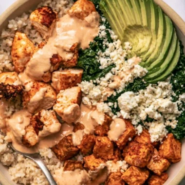 Healthy roasted chicken and sweet potato rice bowl garnished with greens